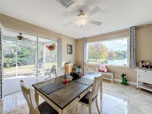 dining room featuring ceiling fan, light tile patterned floors, a water view, and a textured ceiling