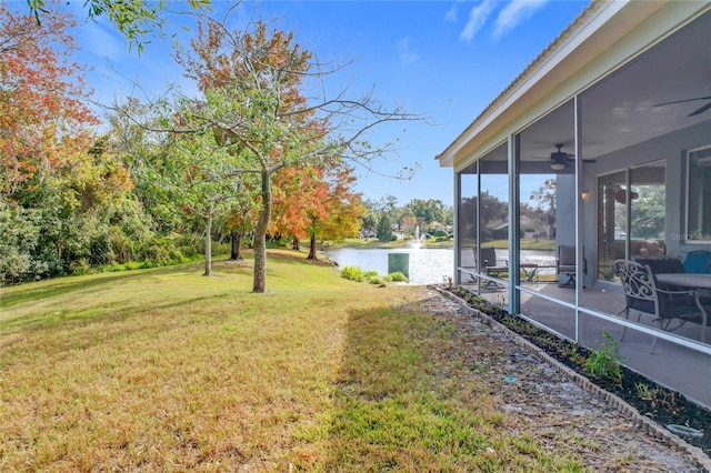 view of yard featuring a sunroom, ceiling fan, and a water view