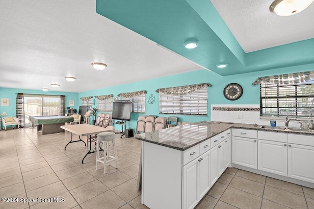 kitchen with light tile patterned flooring, white cabinetry, dark stone countertops, and sink