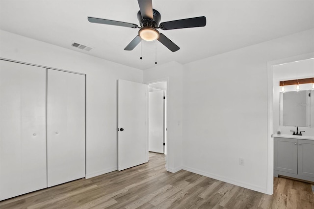 unfurnished bedroom featuring ceiling fan, sink, light hardwood / wood-style flooring, ensuite bathroom, and a closet