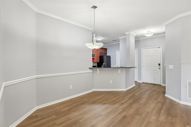 kitchen with black refrigerator, crown molding, light hardwood / wood-style flooring, kitchen peninsula, and a breakfast bar area