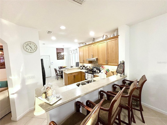 kitchen with backsplash, kitchen peninsula, stainless steel range with electric stovetop, a kitchen bar, and light tile patterned flooring