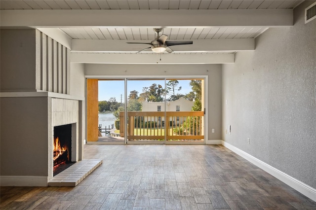 unfurnished living room with beam ceiling, ceiling fan, a brick fireplace, hardwood / wood-style floors, and a water view