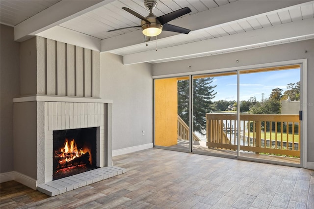 unfurnished living room featuring beam ceiling, ceiling fan, a fireplace, and wood-type flooring