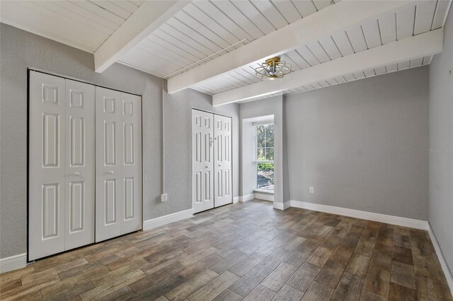 unfurnished bedroom featuring beamed ceiling, wood ceiling, dark wood-type flooring, and multiple closets