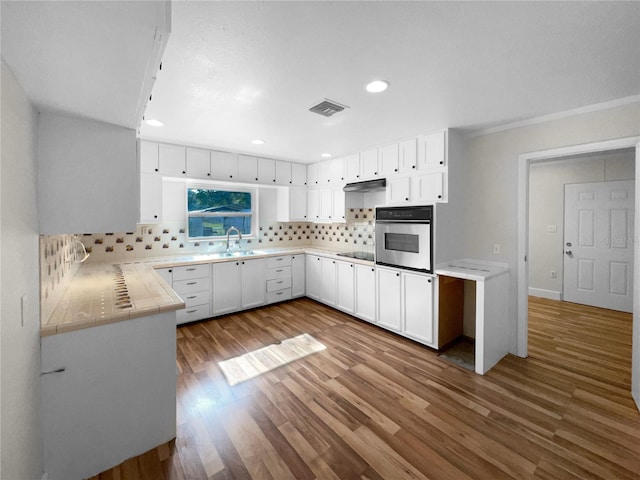 kitchen featuring hardwood / wood-style flooring, oven, white cabinetry, and tasteful backsplash