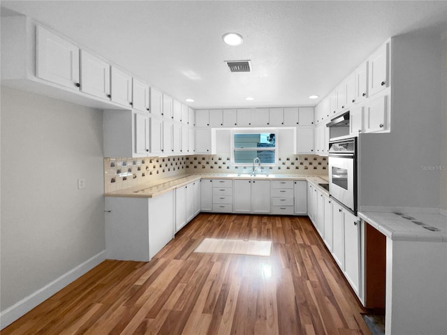 kitchen with white cabinets, decorative backsplash, hardwood / wood-style flooring, and oven