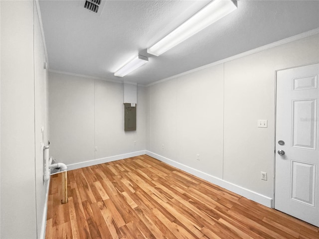 basement featuring electric panel, light hardwood / wood-style flooring, and crown molding