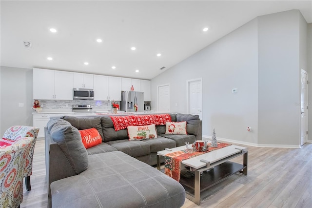 living room with light wood-type flooring, sink, and high vaulted ceiling