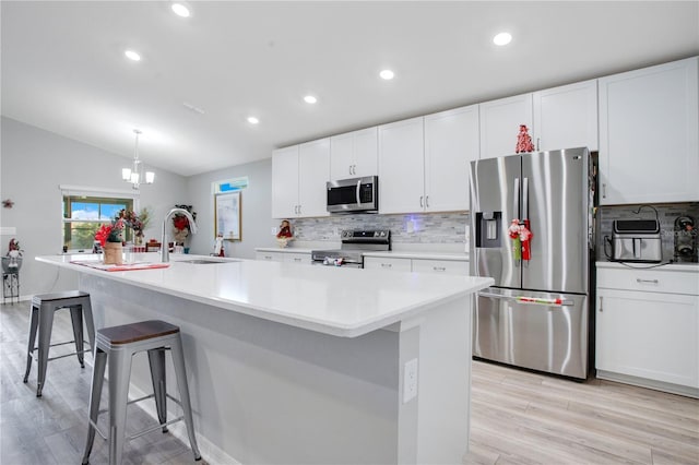 kitchen featuring stainless steel appliances, vaulted ceiling, a kitchen island with sink, sink, and light hardwood / wood-style floors