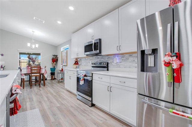 kitchen with light wood-type flooring, stainless steel appliances, vaulted ceiling, an inviting chandelier, and white cabinets