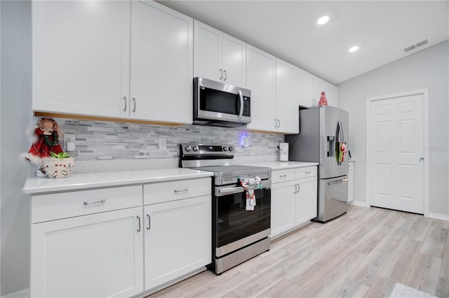 kitchen with backsplash, vaulted ceiling, light hardwood / wood-style floors, white cabinetry, and stainless steel appliances