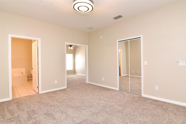 unfurnished bedroom with ensuite bath, a closet, and light colored carpet