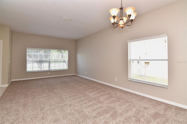 carpeted empty room with a healthy amount of sunlight and an inviting chandelier