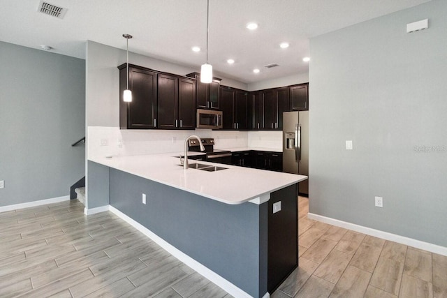 kitchen featuring kitchen peninsula, appliances with stainless steel finishes, sink, pendant lighting, and light hardwood / wood-style flooring