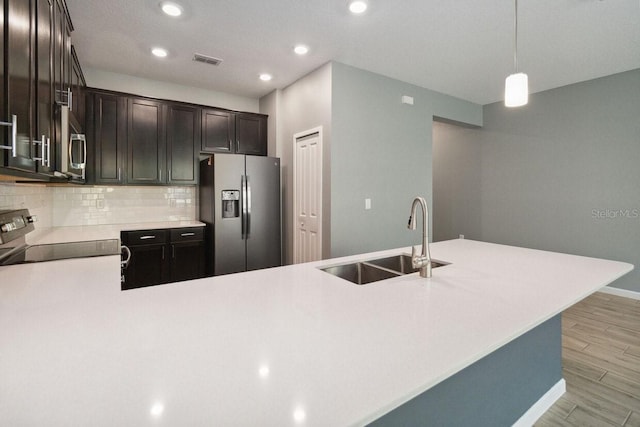 kitchen with sink, stainless steel appliances, backsplash, decorative light fixtures, and light wood-type flooring