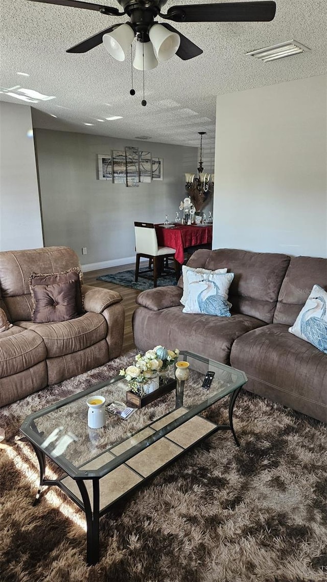 living room featuring ceiling fan with notable chandelier, carpet floors, and a textured ceiling