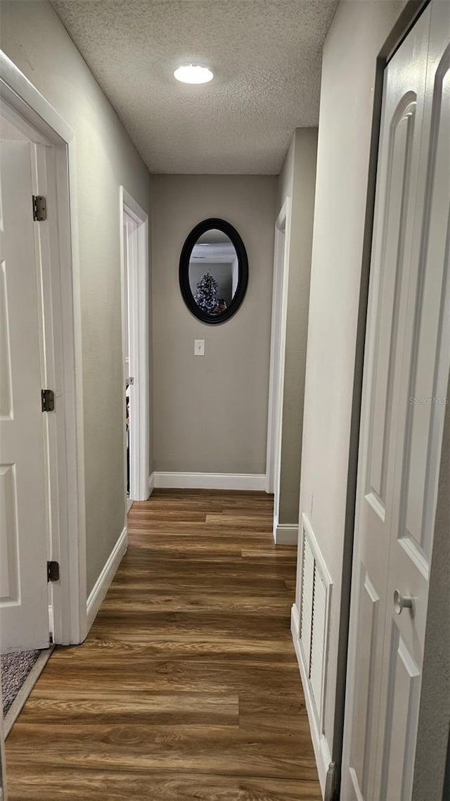 corridor with a textured ceiling and dark hardwood / wood-style flooring