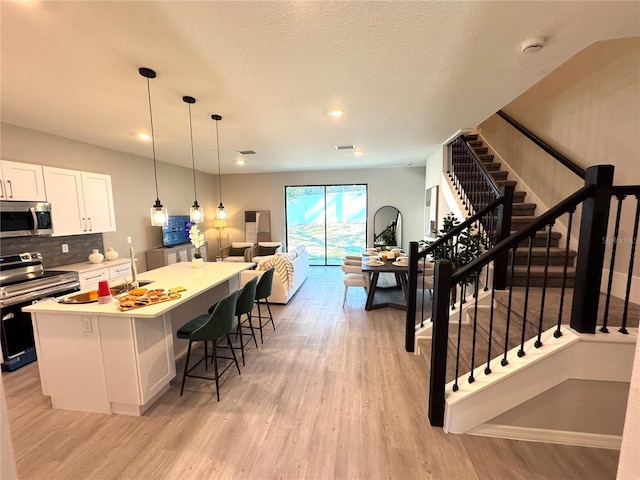 kitchen featuring white cabinets, light wood-type flooring, appliances with stainless steel finishes, a kitchen island, and a breakfast bar area