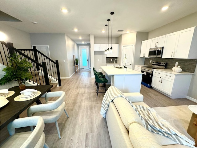 kitchen with a center island with sink, sink, hanging light fixtures, appliances with stainless steel finishes, and white cabinetry