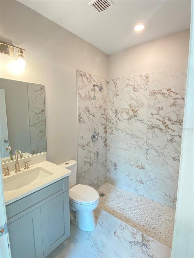 bathroom featuring a tile shower, vanity, and toilet