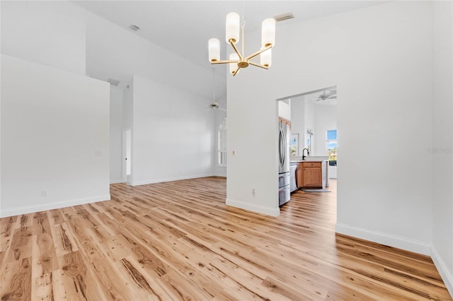 unfurnished living room with light hardwood / wood-style flooring, a towering ceiling, ceiling fan with notable chandelier, and sink