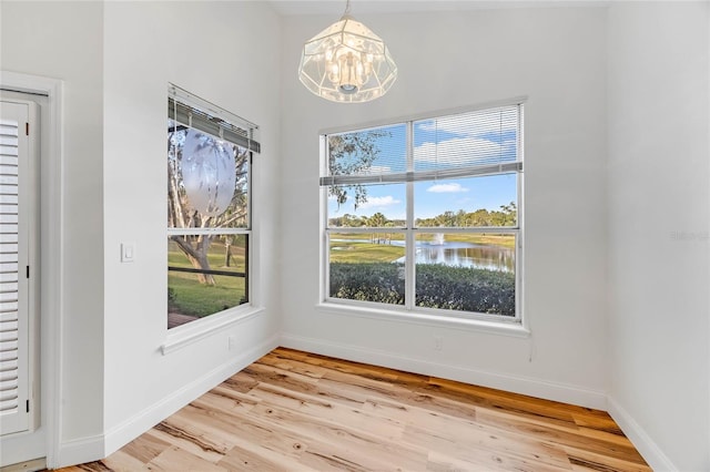 unfurnished dining area with a chandelier, a water view, and light hardwood / wood-style flooring