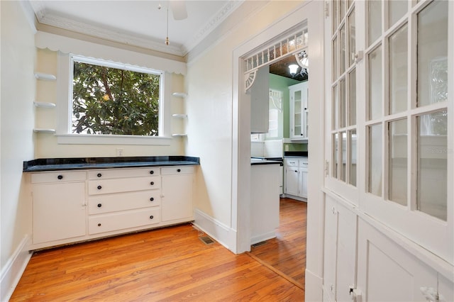 bar with ceiling fan, light wood-type flooring, white cabinetry, and ornamental molding