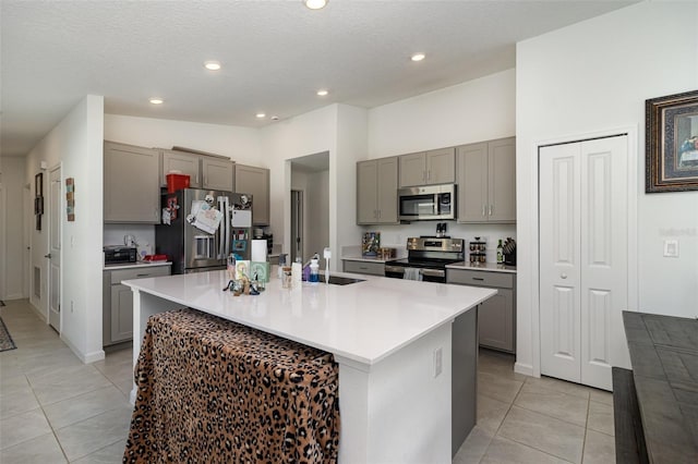 kitchen featuring gray cabinets, a center island with sink, light tile patterned floors, and appliances with stainless steel finishes