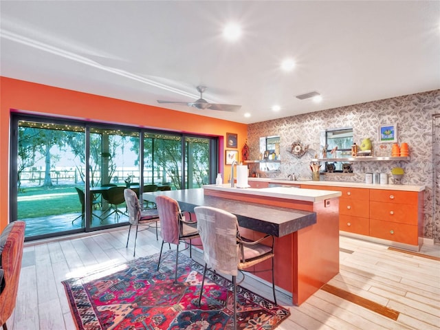 kitchen with ceiling fan, a kitchen breakfast bar, an island with sink, and light wood-type flooring