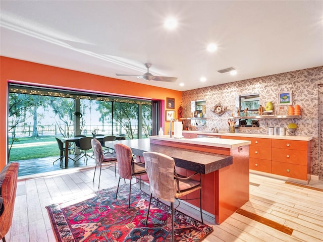 kitchen with an island with sink, a breakfast bar, ceiling fan, and light wood-type flooring