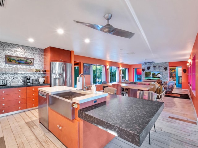 kitchen featuring light hardwood / wood-style flooring, a large island with sink, ceiling fan, stainless steel appliances, and a fireplace