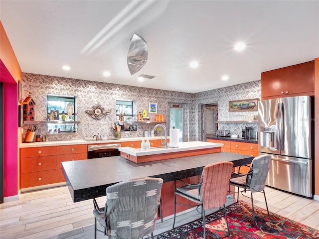 kitchen with dishwasher, sink, stainless steel fridge, a kitchen breakfast bar, and a center island with sink