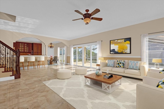 living room with ceiling fan with notable chandelier and crown molding