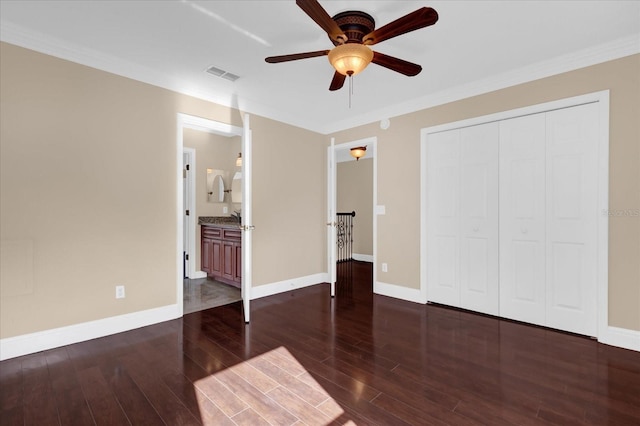 unfurnished bedroom featuring ceiling fan, crown molding, connected bathroom, dark hardwood / wood-style floors, and a closet