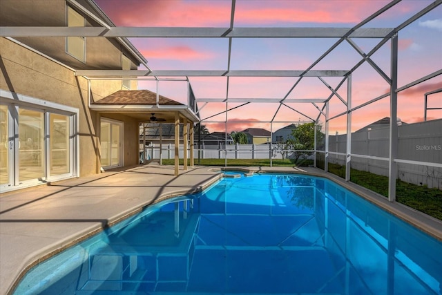 pool at dusk with glass enclosure and a patio area