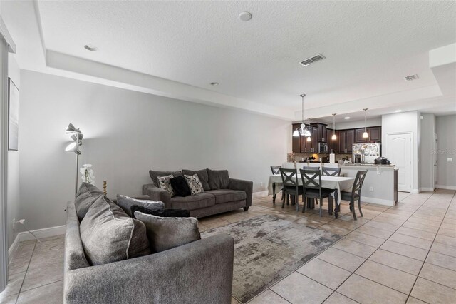 tiled living room featuring an inviting chandelier, a textured ceiling, and a tray ceiling