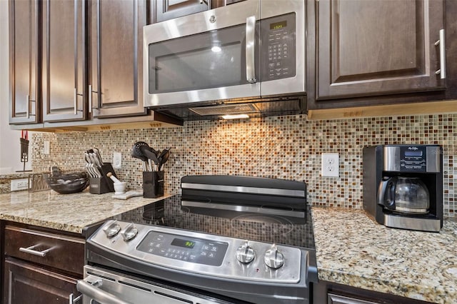 kitchen featuring backsplash, dark brown cabinetry, light stone counters, and appliances with stainless steel finishes