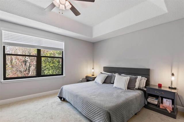 carpeted bedroom with ceiling fan, a textured ceiling, and a tray ceiling