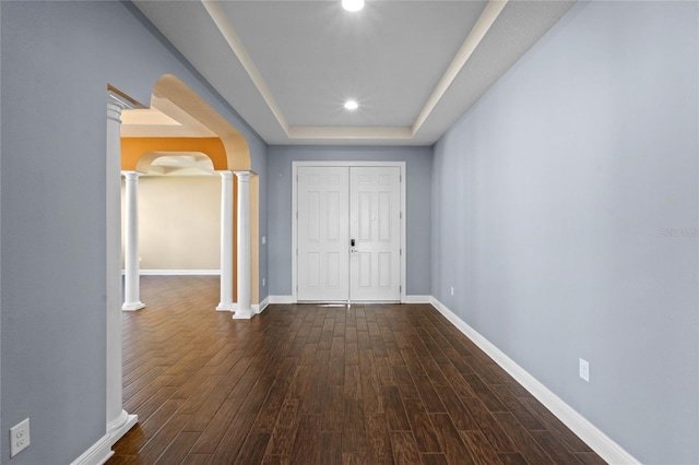 corridor with dark wood-type flooring, a raised ceiling, and ornate columns