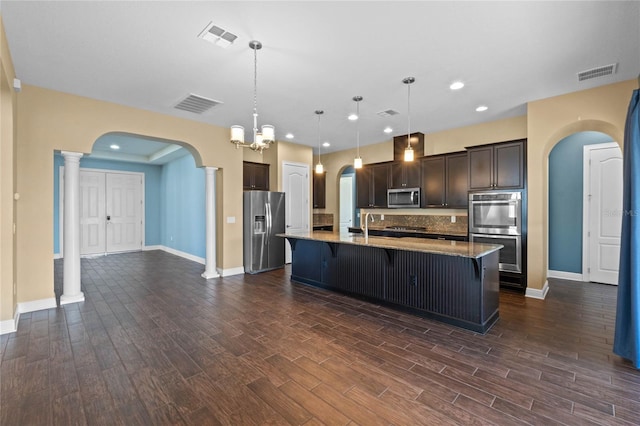 kitchen featuring appliances with stainless steel finishes, decorative light fixtures, dark brown cabinetry, a breakfast bar, and a center island with sink