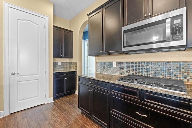 kitchen featuring light stone countertops, dark brown cabinetry, appliances with stainless steel finishes, and decorative backsplash