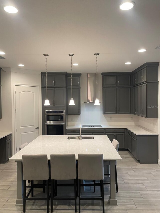 kitchen featuring sink, a center island with sink, hanging light fixtures, and wall chimney range hood