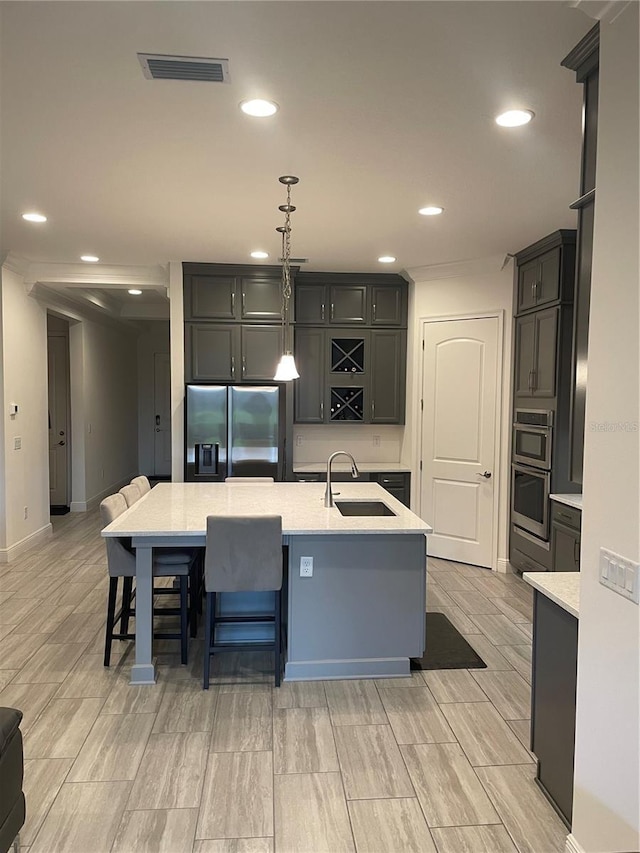 kitchen with a kitchen island with sink, sink, a breakfast bar area, decorative light fixtures, and stainless steel appliances