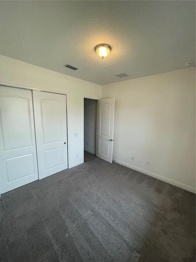 unfurnished bedroom with dark colored carpet, a textured ceiling, and a closet