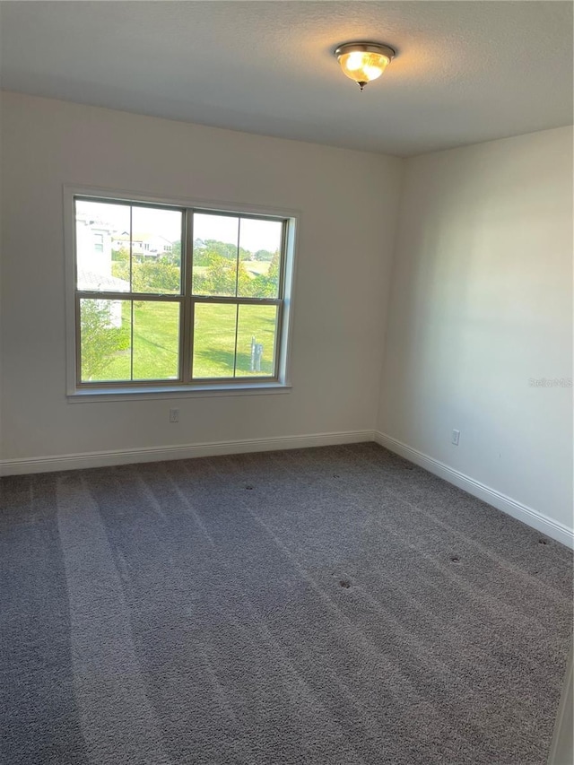 empty room featuring dark colored carpet and plenty of natural light