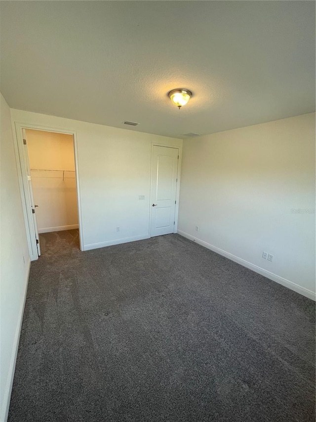 unfurnished bedroom featuring a walk in closet, a closet, dark carpet, and a textured ceiling