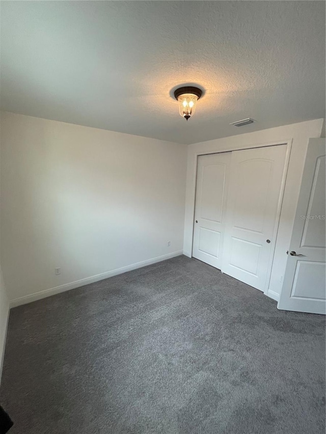 unfurnished bedroom featuring dark colored carpet, a textured ceiling, and a closet