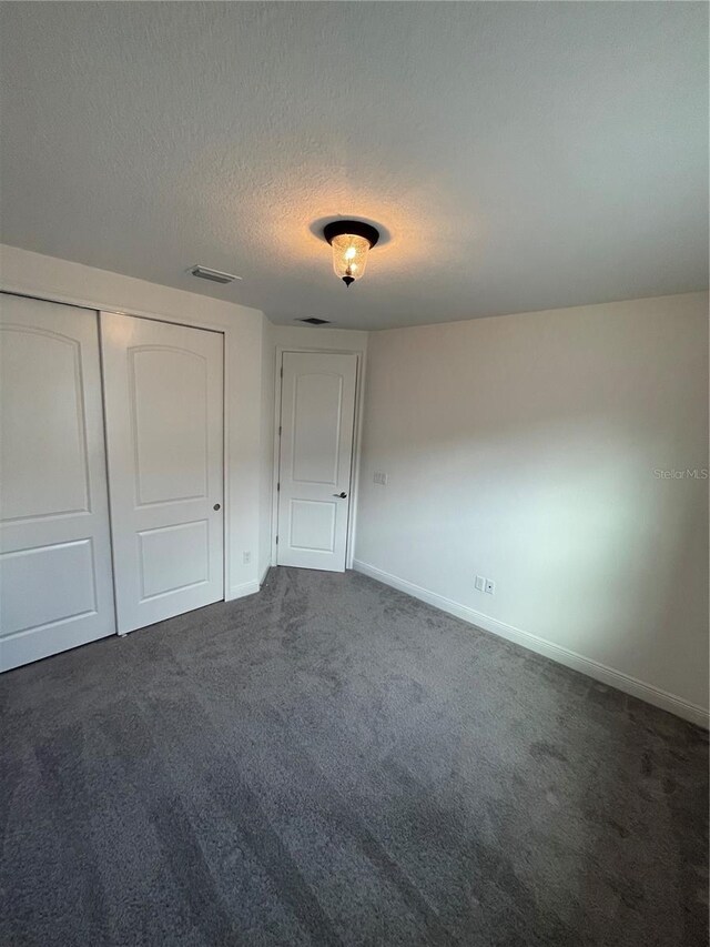 unfurnished bedroom featuring a closet, dark carpet, and a textured ceiling