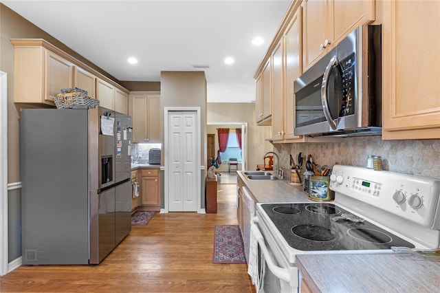 kitchen featuring sink, decorative backsplash, light brown cabinetry, appliances with stainless steel finishes, and light hardwood / wood-style floors